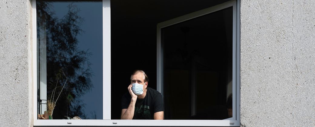 Un hombre con barbijo mira por la ventana de su departamento. Créditos: Shutterstock