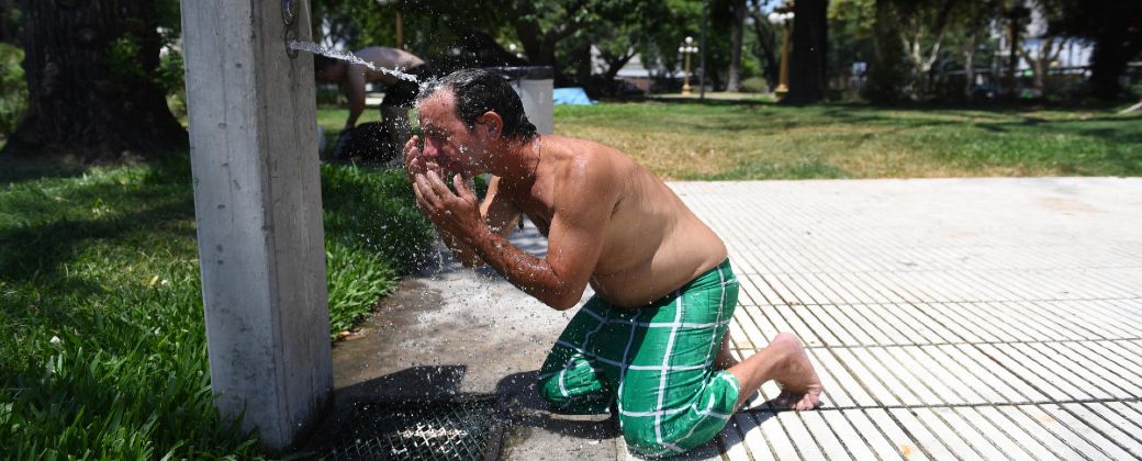 Con el torso desnudo, un hombre se arrodilla para mojarse la cabeza con agua. Créditos: Maximiliano Luna / Infobae