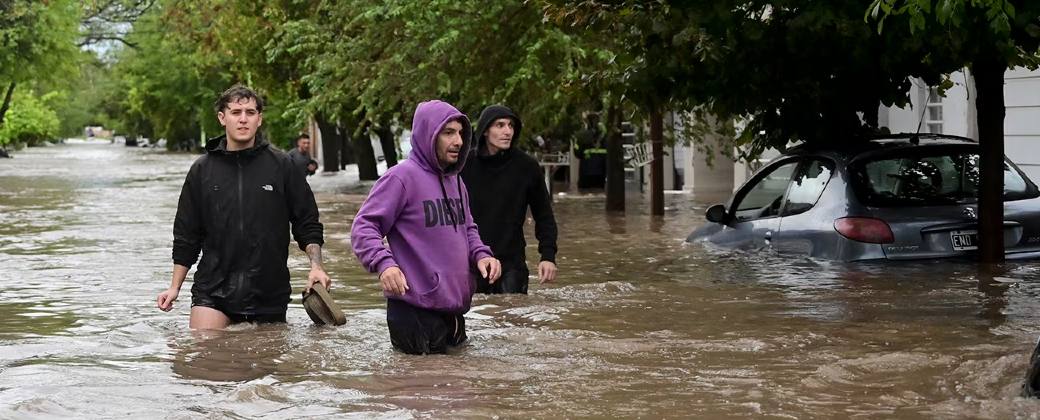 Tres hombres caminan por las calles inundadas de Bahía Blanca después de la tormenta. Créditos: AP