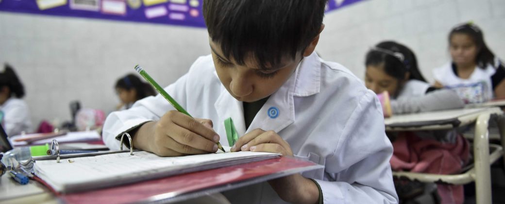 Un niño de escuela primaria escribe en su carpeta. Créditos: Argentina.gob.ar